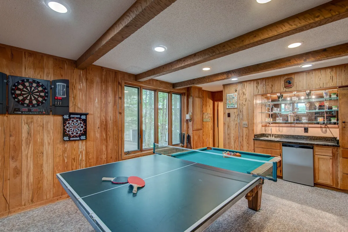 A vibrant recreational space with a ping pong table set up as the focal point, dart boards mounted on the wall, a window letting in natural light, and a bar area visible nearby. The area exudes energy and is perfect for friendly matches and socializing.