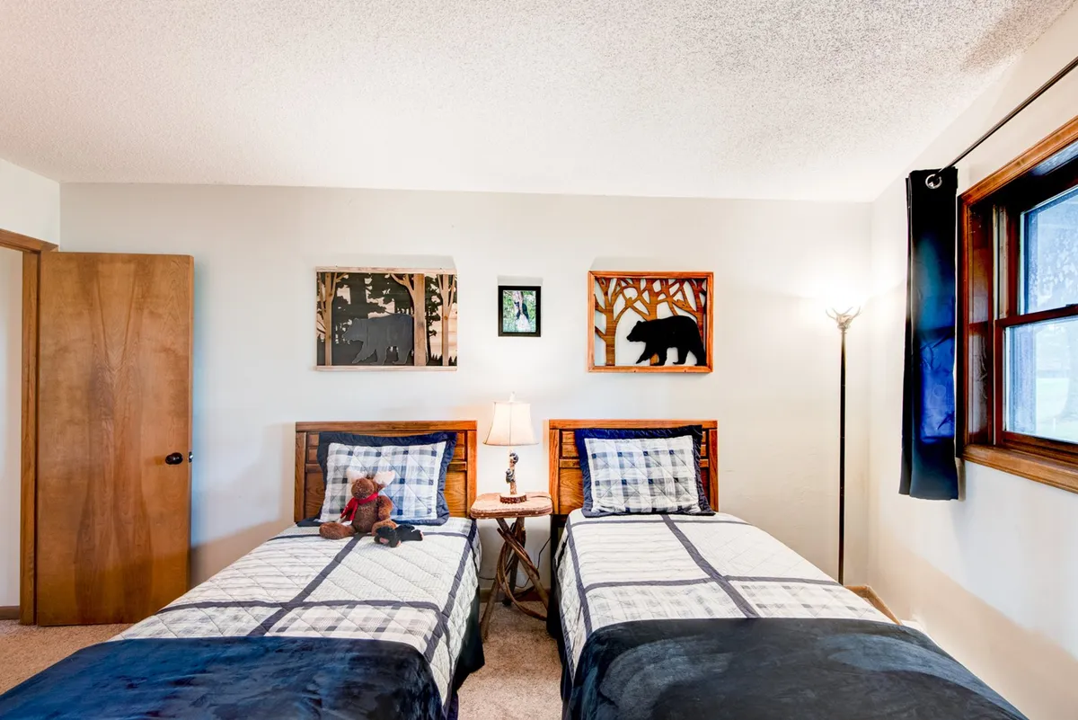 A cheerful twin bedroom displaying two twin beds with bear-themed wall art and a table lamp between the beds. The playful decor and inviting setup make it especially appealing for children or friends, emphasizing comfort and togetherness.