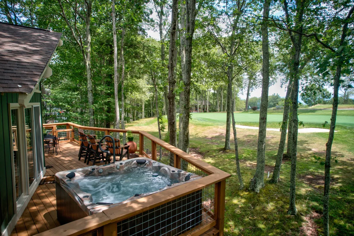 A tranquil scene of a hot tub positioned on the deck with seating, overlooking the manicured golf course. The image conveys a sense of privacy and peacefulness, ideal for unwinding after a day on the course or exploring Beech Mountain. The composition emphasizes the direct relationship between the relaxation amenities and the scenic views beyond.