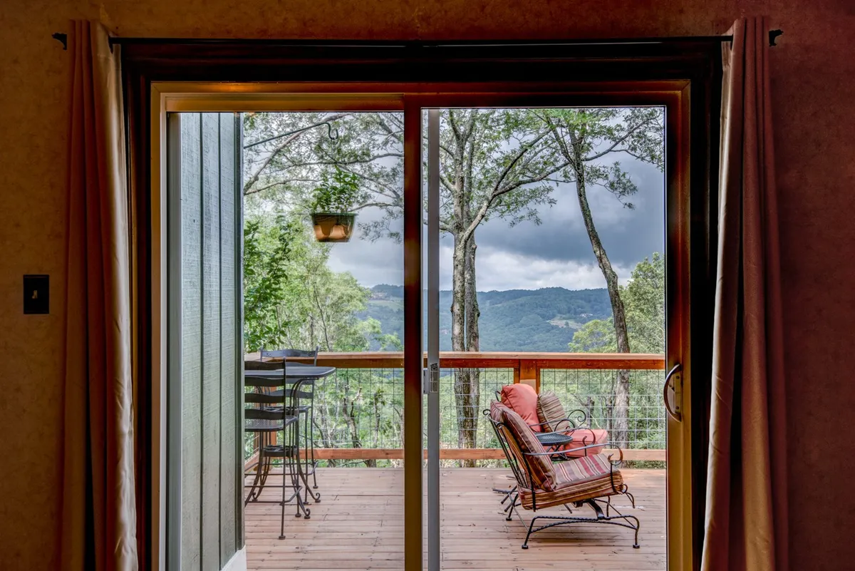 Interior view looking through a sliding glass door toward an outdoor seating area and mountain vistas beyond. The setup allows for seamless indoor-outdoor living and frames the perfect spot for sipping coffee or wine while watching the sunset over the ridges.