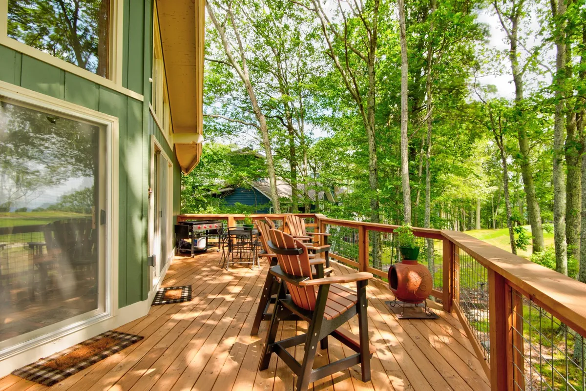 A cozy outdoor living area featuring a wooden deck, comfortable seating, a fire pit, and a backdrop of leafy trees. The space is perfect for relaxing after a day’s exploration, gathering for family games, or enjoying the mountain air with loved ones.