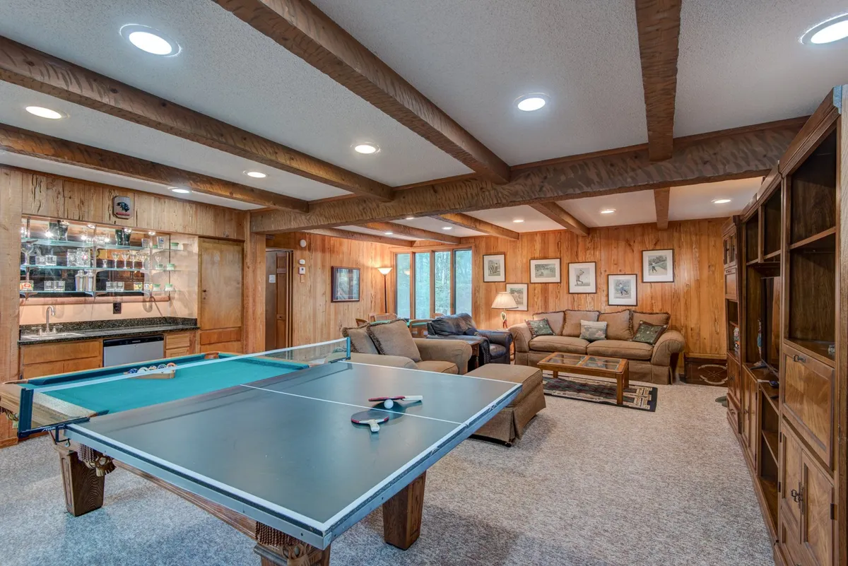 An inviting game room scene featuring a ping pong table, a comfortable seating area, a wet bar for refreshments, and framed artwork adding personality to the space. The atmosphere is friendly and designed for relaxing or entertaining.